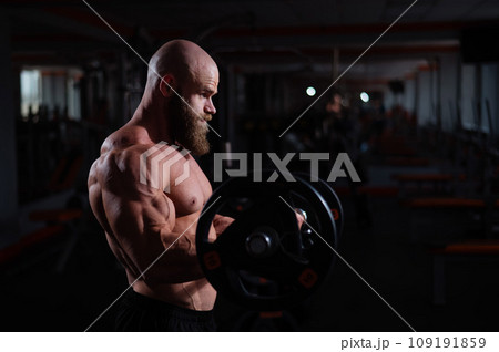 Caucasian bald topless man doing an exercise with a barbell in the gym. Bicep curls with weights. Caucasian bald topless man doing an exercise with a barbell in the gym. Bicep curls with weights. 109191859