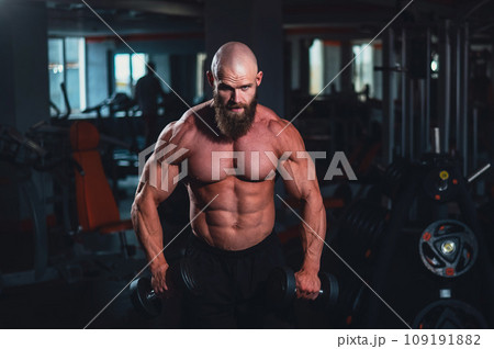 A muscular shirtless man lifts dumbbells to the sides with dumbbells in the gym. 109191882