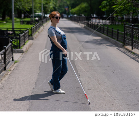 Blind pregnant woman crosses the street with the help of a tactile cane. 109193157