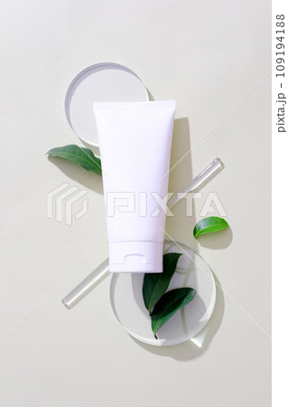 Close-up of a cosmetic tube placed on two glass platforms, green tea leaves decorated around, and a glass rod. Exquisite mockup for natural cosmetics advertising. Close-up of a cosmetic tube placed on two glass platforms, green tea leaves decorated around, and a glass rod. Exquisite mockup for natural cosmetics advertising. 109194188
