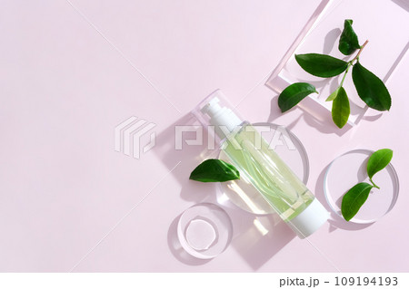 Hair spray bottles with green tea extract are displayed with fresh green tea leaves and transparent glass podiums on a pastel background. Mockup for vegan cosmetics advertisement. Hair spray bottles with green tea extract are displayed with fresh green tea leaves and transparent glass podiums on a pastel background. Mockup for vegan cosmetics advertisement. 109194193