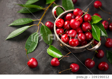Cherry summer background. A large number of cherries with leaves on the table in a saucepan on a black background. close-up. 109196012