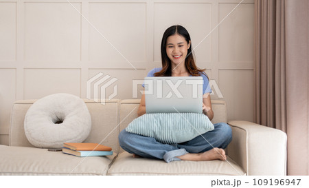 Young pretty Asian woman using laptop computer while sitting on the sofa in her living room. 109196947