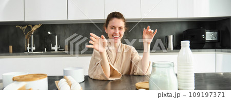 Attractive young cheerful girl baking at the kitchen, making dough, holding recipe book, having ideas 109197371