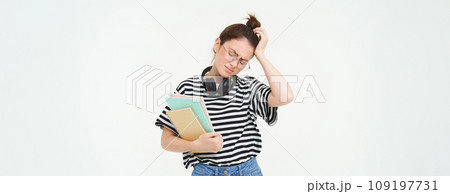 Disappointed young woman, looking tired or upset, wearing glasses, holding study material, documents and notebooks, stands over white background Disappointed young woman, looking tired or upset, wearing glasses, holding study material, documents and notebooks, stands over white background 109197731