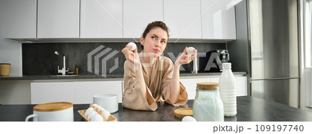 Attractive young cheerful girl baking at the kitchen, making dough, holding recipe book, having ideas Attractive young cheerful girl baking at the kitchen, making dough, holding recipe book, having ideas 109197740