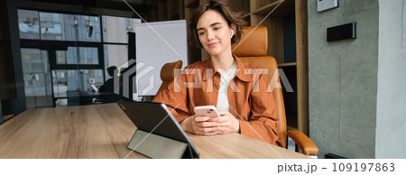 Portrait of female employee, start up entrepreneur in office, working with digital tablet, sitting in conference room waiting for team meeting 109197863
