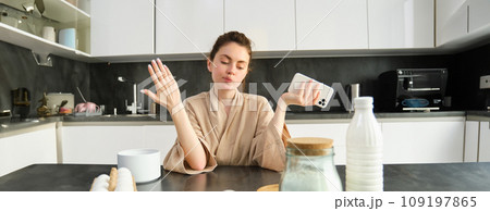 Attractive young cheerful girl baking at the kitchen, making dough, holding recipe book, having ideas Attractive young cheerful girl baking at the kitchen, making dough, holding recipe book, having ideas 109197865