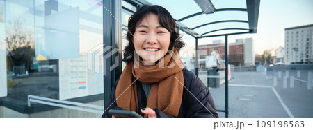 Beautiful young woman, standing on bus stop, waiting for her public transport, using mobile phone, using smartphone application 109198583