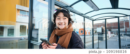 Beautiful young woman, standing on bus stop, waiting for her public transport, using mobile phone, using smartphone application Beautiful young woman, standing on bus stop, waiting for her public transport, using mobile phone, using smartphone application 109198816
