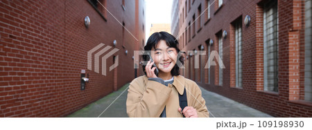 Portrait of young korean woman walking down street with phone, talking with someone, makes a call, has telephone conversation Portrait of young korean woman walking down street with phone, talking with someone, makes a call, has telephone conversation 109198930