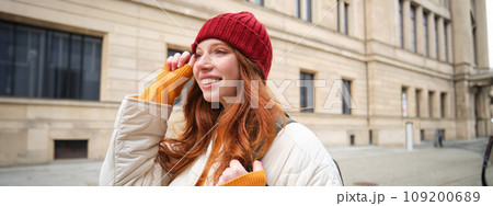 Tourism and travelling. Young redhead woman smiling, tourist walking with backpack around city centre, sightseeing, holds backpack with paper map 109200689