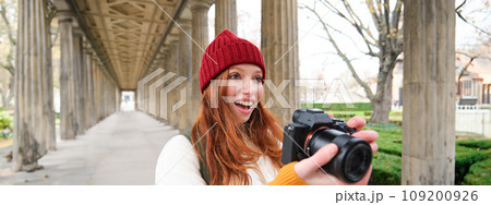 Smiling tourist photographer, takes picture during her trip, holds professional camera and makes photos Smiling tourist photographer, takes picture during her trip, holds professional camera and makes photos 109200926