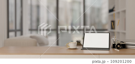 A digital tablet mockup, a camera, a coffee cup, and books on a wooden table in a modern room. 109201200
