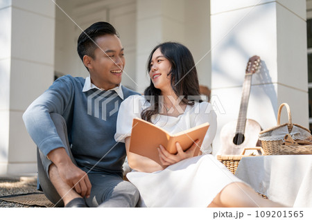 Lovely sweet young Asian couple enjoying picnic on a sunny day at home together, reading a book 109201565