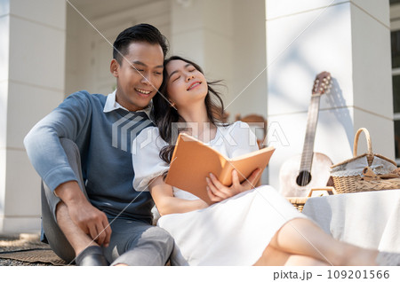 Lovely sweet young Asian couple enjoying picnic on a sunny day at home together, reading a book 109201566
