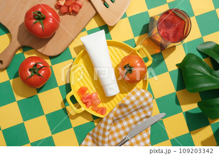 Beauty product mockup displayed on yellow ceramic pan with fresh tomatoes, glass of tomato juice, wooden tray and green leaf. Green and yellow checkered background for creative advertising 109203342