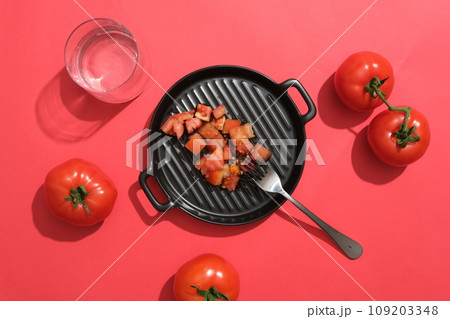 Tomato slices are decorated on a black pan with a fork, surrounded by fresh ripe tomatoes on a red background. Tomatoes contain many nutrients that are good for health. Top view, advertising photo 109203348