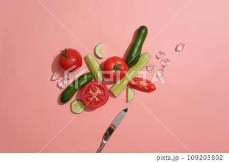 Cucumber and tomato cut in slices and halves decorated over pink background with ice cubes and a knife. Concept of healthy fruits that good for skin and health Cucumber and tomato cut in slices and halves decorated over pink background with ice cubes and a knife. Concept of healthy fruits that good for skin and health 109203802