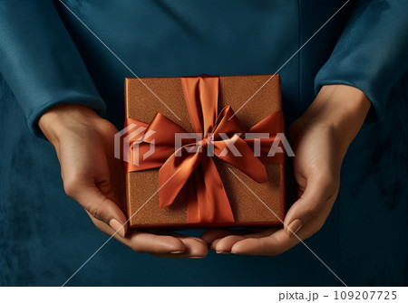 Woman hand holding a gift with gold ribbon bow on blue background 109207725