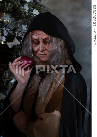 Stepmother witch gives poisoned red apple.Woman as witch in black offers red apple as symbol of temptation, poison. Fairy tale, white snow wizard concept. Spooky Halloween, cosplay. 109207988