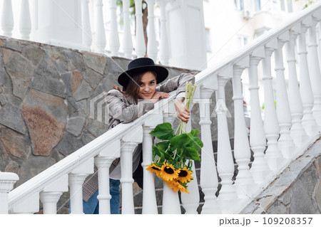 Woman in a hat with flowers on a walk near the railing Woman in a hat with flowers on a walk near the railing 109208357