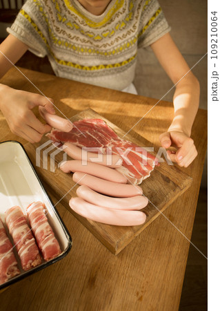 A girl prepares a traditional Christmas dish "Pigs in a blanket" Wraps sausages in bacon 109210064