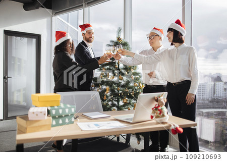 Multiethnic business people in Santa hats clinking champagne with colleagues 109210693