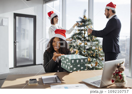 Portrait of african businesswoman in suit and Santa hat presenting surprise gift 109210757