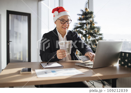 asian male accountant in Santa hat holding cash banknotes. 109212839