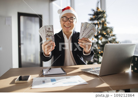 Asian man in Santa hat showing hands with cash papers counting money 109212864