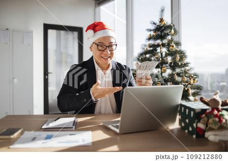 Adult asian rich business man in Santa hat working on laptop counting money cash 109212880