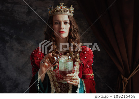 insidious medieval queen in dress pouring poison into goblet 109215458