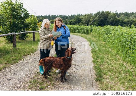 Two happy Womans in active trekking clothes with map having a halt after hiking. Travel and active lifestyle concept, full body. Travel and hiking with pet. Two happy Womans in active trekking clothes with map having a halt after hiking. Travel and active lifestyle concept, full body. Travel and hiking with pet. 109216172