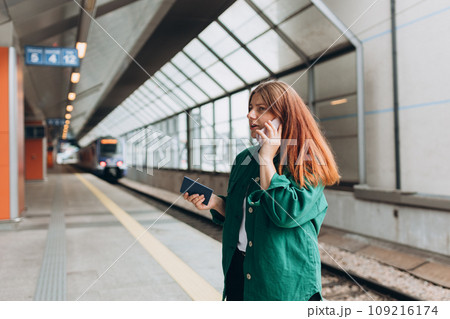 Young worried redhead woman waiting train on station platform, she lost or late, unhappy girl talking on smart phone. Railroad transport concept, Communication banner 109216174