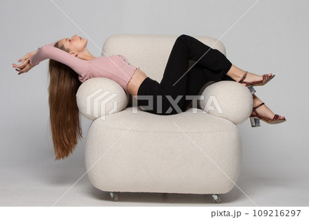 A beautiful slender girl with long blond hair lies in a comfortable white chair. A woman rests and relaxes in a chair. 109216297