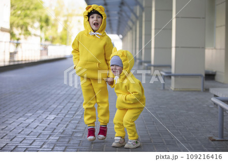 Little brother and sister. Funny children boy and girl in yellow suits jump and laugh. 109216416