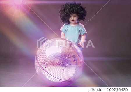 A little funny girl looks with admiration at a shiny pink disco ball. 109216420