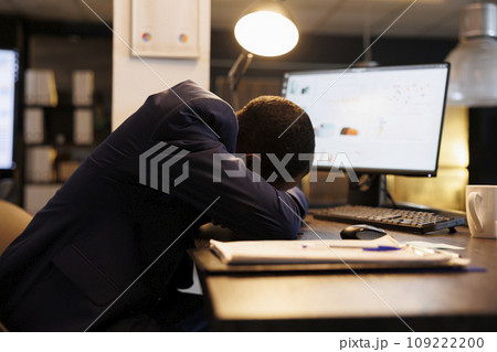 Workaholic businessman slepping desk in startup office, after checking marketing statistics on computer. Exhausted tired entrepreneur working overtime at company strategy plan. Business concept 109222200