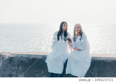 海辺でスマホを見る若い女性2人の写真 109223721