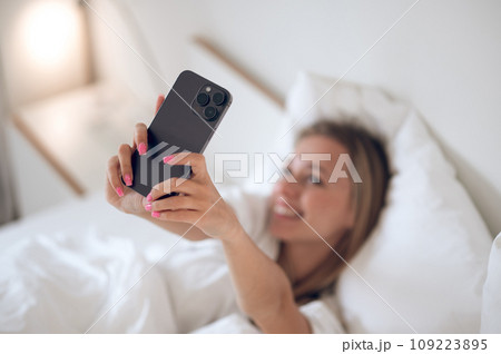 Young girl lying in bed and holding a smartphone in hands 109223895