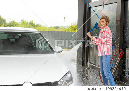 Young woman washing the car at the car wash and looking involved Young woman washing the car at the car wash and looking involved 109224056