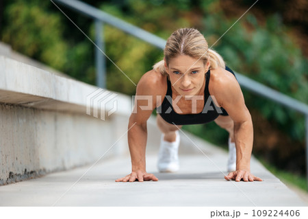 Blonde woman doing push ups outdoor. 109224406