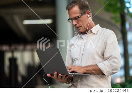 Middle aged man using laptop computer on city street. 109224448