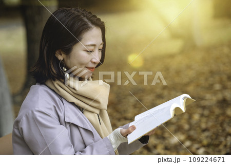 紅葉の公園のベンチで読書をする女性 109224671