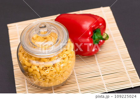 Uncooked Chifferi Rigati Pasta in Glass Jar with Red Bell Pepper on Bamboo Mat 109225024