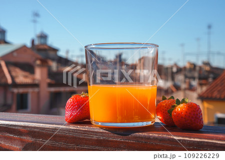 A refreshing glass of orange juice with strawberries sits on a neutral-toned balcony. This image is part of a collection showcasing popular places in Venice, Italy. 109226229
