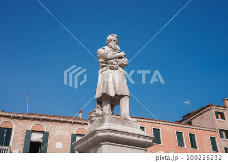 A striking statue of a man in a long coat and hat stands in front of a building in Venice, Italy, adding to the city's rich history and charm. A striking statue of a man in a long coat and hat stands in front of a building in Venice, Italy, adding to the city's rich history and charm. 109226232