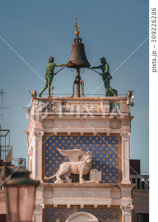 Aerial view of lion statue and bell on a building in Venice, Italy. The lion is a common symbol in Venetian culture, adding historical and architectural significance to the unique structure. Aerial view of lion statue and bell on a building in Venice, Italy. The lion is a common symbol in Venetian culture, adding historical and architectural significance to the unique structure. 109226286