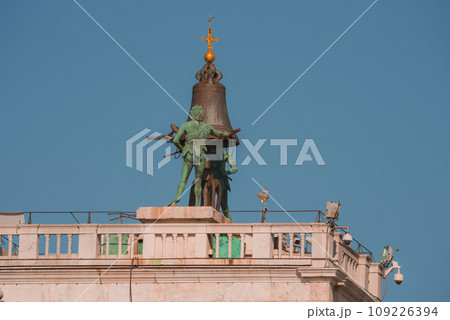 Statue of person in white robe holding sword and bell on top of building in Venice, Italy. Architectural style not specified. Statue of person in white robe holding sword and bell on top of building in Venice, Italy. Architectural style not specified. 109226394